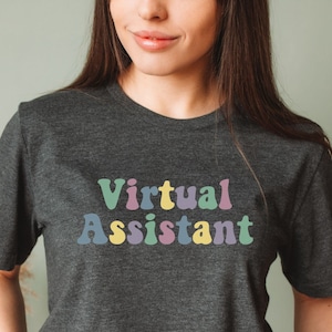 May include: A dark gray t-shirt with the text "Virtual Assistant" in colorful, retro-style lettering.
