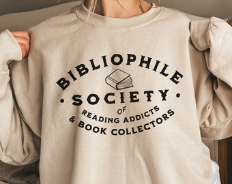May include: A beige sweatshirt with a black graphic print that reads "Bibliophile Society of Reading Addicts & Book Collectors" with an illustration of a book.
