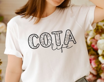 May include: White t-shirt with black text that says "COTA life" with a floral design inside the letters.