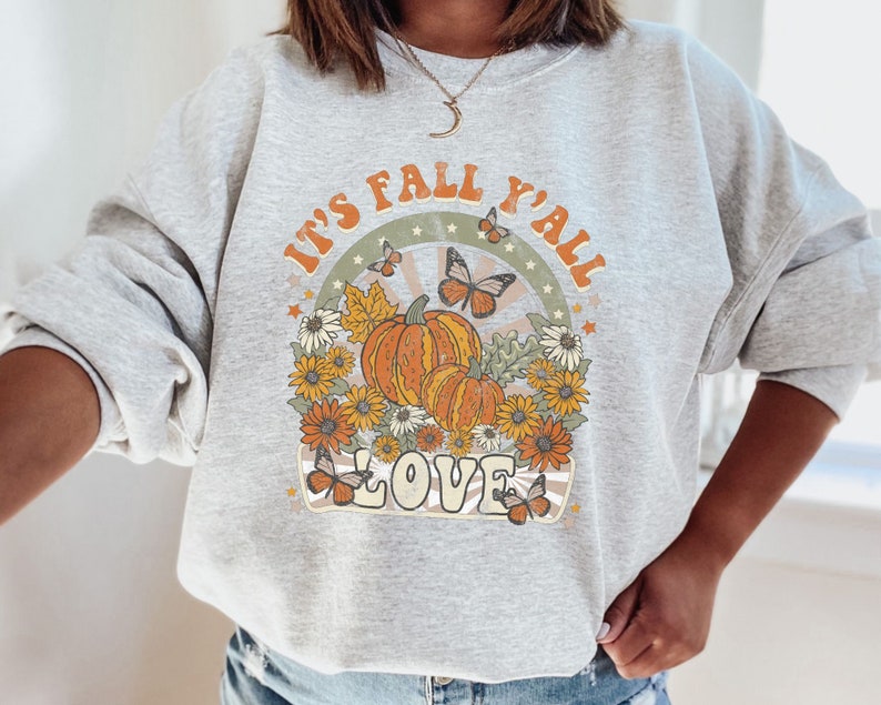 Pode incluir: Uma camisa de moletom cinza com uma estampa gr&aacute;fica retr&ocirc; que diz "It's Fall Y'all Love" com ab&oacute;boras, borboletas e flores.
