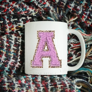 May include: White ceramic mug with a pink and gold glitter letter A on the front. The mug has a handle and the text "Lil Rose Petals" is printed on the bottom.