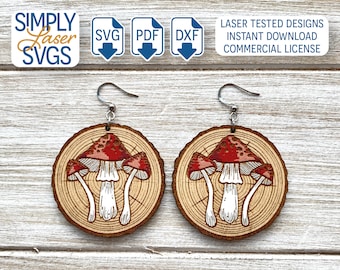 May include: A pair of wooden earrings with a mushroom design. The earrings are round and have a wood grain pattern. The mushrooms are red with white spots and white stems. The earrings are attached to silver hooks.