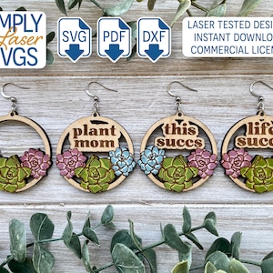 May include: Wooden earrings with a circular design, featuring a succulent plant motif in green, pink, and blue. The earrings have the phrases "plant mom", "this succs", and "life succs". The image also includes the text "SIMPLY Laser SVGS".