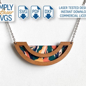 Puede incluir: Un collar de madera con un colgante semicircular de doble capa. El colgante está hecho de dos piezas de madera, con un patrón floral colorido visible a través de las secciones recortadas. El collar está en una cadena plateada.