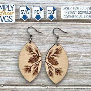 May include: A pair of wooden earrings with a laser-cut design of pine branches and pine cones. The earrings are oval-shaped and have silver hooks.