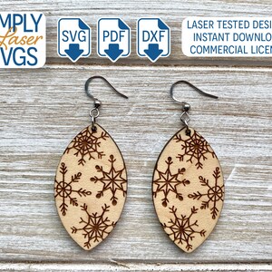 May include: A pair of wooden earrings with a snowflake design. The earrings are oval shaped and have a silver hook.