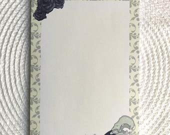 Può includere: Un blocco note vuoto con un bordo decorativo che presenta un motivo floreale in grigio e uno sfondo giallo chiaro. L'angolo superiore presenta un gruppo di tre rose nere. L'angolo inferiore presenta un teschio di uccello grigio e bianco con un becco nero. Il blocco note ha il testo "wind & Maxine" stampato in grigio in basso.