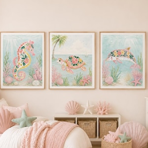 Op de afbeelding: Drie ingelijste kunstprints met zeedieren: een zeepaardje, een schildpad en een dolfijn, elk versierd met bloemmotieven. Het kunstwerk is geplaatst tegen een lichtblauwe achtergrond met koraal- en zeewieraccenten. De kamer is ingericht in zachte roze en witte tinten.