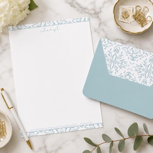 May include: A white stationery sheet with a light blue floral border, the name "cheryl" printed at the top, and the text "GIVE THANKS TO THE LORD FOR HE IS GOOD. PSALM 107:1" at the bottom, paired with a matching light blue envelope with a floral liner.
