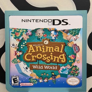 May include: A blue Nintendo DS game case featuring a colourful image of the game Animal Crossing: Wild World. The game depicts a cartoon world with animals and a clock. The game case has an "E" rating from the ESRB.