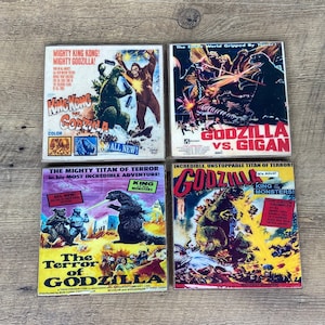 May include: Four vintage movie posters featuring Godzilla, King Kong, and Gigan. The posters are colorful and feature images of the monsters in action. The text on the posters includes the titles of the movies, the names of the monsters, and the release dates.