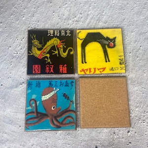 May include: Four square coasters with Japanese-inspired designs. One features a black cat on yellow, another a dragon on black, and a third an octopus on blue. The fourth coaster is plain cork.