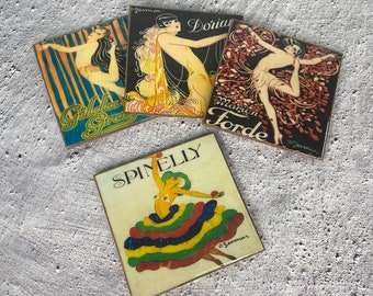 May include: Four vintage-style coasters featuring images of women in various poses. The coasters are square and have a gold border. The images are in a retro art style and feature bright colors. The coasters feature the names "Gilda Gray", "Dorian", "Marion Torde", and "Spinelly".