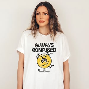 Puede incluir: Camiseta blanca con una cara de dibujos animados amarilla y el texto "ALWAYS CONFUSED".