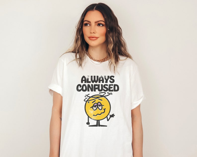 Puede incluir: Camiseta blanca con una cara de dibujos animados amarilla y el texto "ALWAYS CONFUSED".