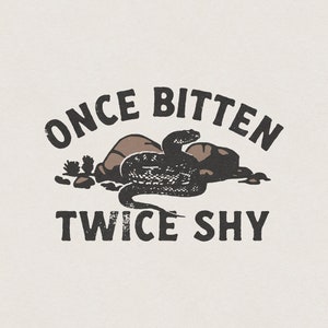 Op de afbeelding: Zwart-wit grafisch ontwerp met een slang die om rotsen is gewikkeld. De tekst "Once Bitten Twice Shy" is geschreven in een vintage lettertype.