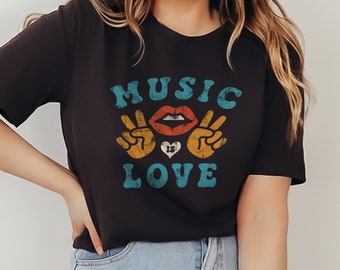 May include: A black t-shirt with a vintage-style graphic that says "MUSIC IS LOVE" in blue and yellow lettering. The graphic also includes a red lip, a heart, and two peace signs.