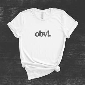 May include: White t-shirt with the word "obvi." printed in black on the front.