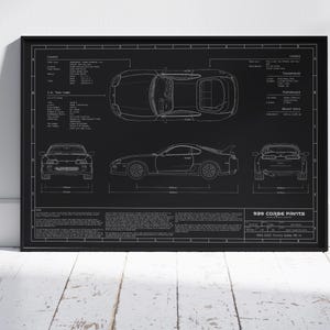 May include: Black framed blueprint-style print featuring a Toyota Supra. The print shows top, side, front, and rear views of the car, along with technical specifications and the text "939 Corse Prints".