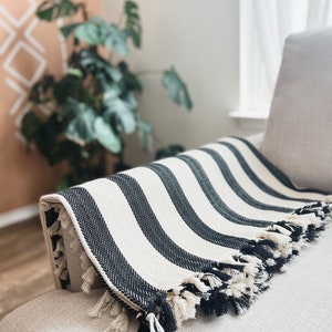 May include: Black and white striped throw blanket with fringe on a white sofa.