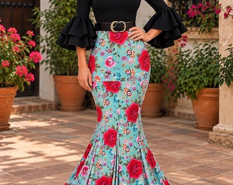 Op de afbeelding: Een vloerlange jurk met een zwart lijfje met V-hals, driekwartmouwen met gelaagde ruches en een turquoise rok met een levendige rode bloemenprint. De taille is ingesnoerd met een zwarte riem met een goudkleurige gesp.
