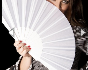 May include: A white, open hand fan with a pleated design. The fan is held in front of a person's face, with only their eyes visible. The person is wearing a black and white polka dot top with a white lace trim.