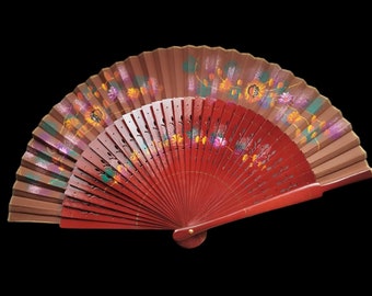 May include: A decorative hand fan with a red and brown color scheme. The fan is open, revealing a painted floral design in shades of purple, yellow, and green. The fan's wooden frame is visible.