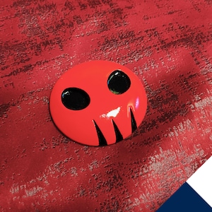 May include: A red and black skull-shaped pin with two black eyes. The pin is glossy and has a 3D effect.