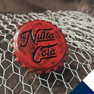 May include: Red bottle top with the words "Nuka Cola" in black lettering. The top is on a wire mesh background.