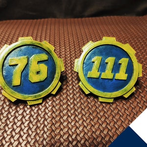 May include: Two Fallout Vault-Tec style badges, one with the number 76 and the other with the number 111. The badges are yellow and blue with a gear design around the edges.