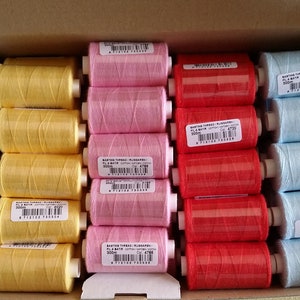 Può includere: Una scatola di 40 bobine di filo di vari colori, tra cui bianco, giallo, rosa, rosso e blu. Ogni bobina è etichettata con il nome del marchio e la lunghezza del filo.