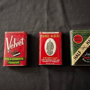 May include: Three vintage tobacco tins. The first tin is red and says "Velvet Pipe & Cigarette Tobacco". The second tin is red and says "Prince Albert Crimp Cut Long Burning Pipe and Cigarette Tobacco Net Wt. 1 1/2 oz.". The third tin is green and says "Burley Bright Genuine Half and Half A Cargo of Contentment in the Bowl of Any Pipe".