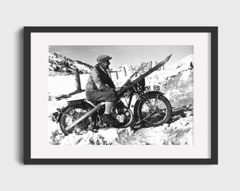 May include: A black and white photograph of a person riding a motorcycle in the snow. The motorcycle has a license plate that reads "DV 690". The person is wearing a hat and is holding a pair of skis.