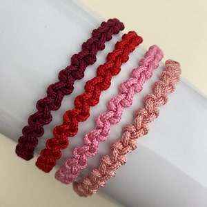 May include: Four braided bracelets in shades of pink and red. The bracelets are made of a soft, woven material and are tied together in a knot.