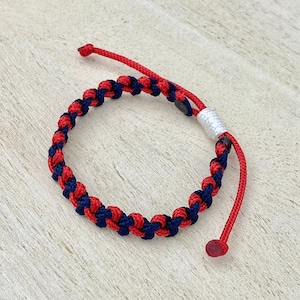 May include: A red and navy blue braided bracelet with a white bead accent.