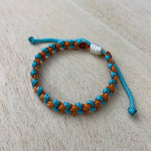 May include: A braided bracelet with blue and orange cord, tied with a white knot.