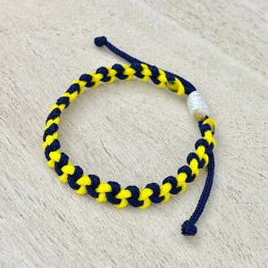 May include: A yellow and navy blue braided bracelet with a white bead accent.