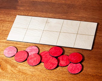 Puede incluir: Un tablero de juego de madera con una cuadrícula de cuadrados y un conjunto de piezas de juego circulares rojas. El tablero es rectangular y está hecho de madera clara. Las piezas rojas están esparcidas alrededor del tablero.