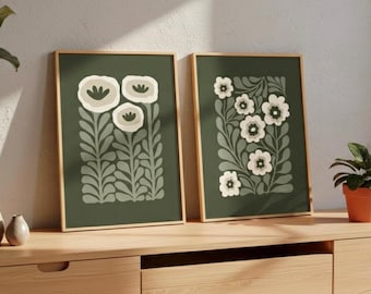Può includere: Due stampe artistiche floreali incorniciate. Ogni stampa presenta uno sfondo verde scuro con fiori e foglie bianche e verde chiaro stilizzati. Le cornici sono di colore legno chiaro. Le stampe sono esposte su un mobile in legno.