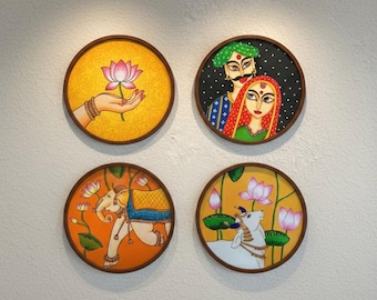 May include: Four round wall art pieces with brown frames. Each piece features a different Indian-inspired illustration: a hand holding a lotus flower, a couple, an elephant, and a cow with lotus flowers.