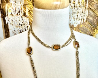 May include: A gold chain necklace with three strands and three large, rectangular, amber-colored stones. The necklace is layered and has a long, dangling chain.