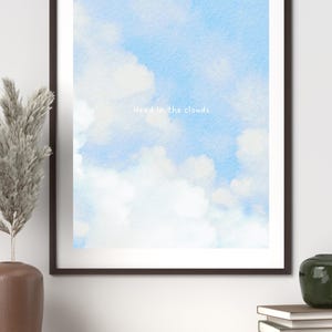 Könnte beinhalten: Gerahmter Kunstdruck mit einem Aquarellhimmel mit weißen Wolken auf hellblauem Hintergrund. Der Satz "Head in the clouds" ist in weißer Schrift geschrieben. Das Kunstwerk wird in einem dunkelbraunen Rahmen präsentiert.