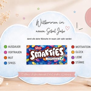 Op de afbeelding: Een wolkvormige kaart met de tekst Willkommen im neuen Schul Jahr en een pakje Nestle Smarties. De kaart bevat een lijst met Duitse woorden zoals Ausdauer, Vertrauen, Mut, Spass, Motivation, Glück, Liebe en Stärke naast gekleurde stippen.