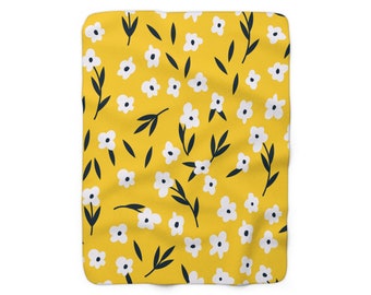Könnte beinhalten: Eine gelbe Fleece-Decke mit einem weißen Blumenmuster. Die Blumen sind zufällig über die Decke verteilt und haben einen einfachen, handgezeichneten Stil.