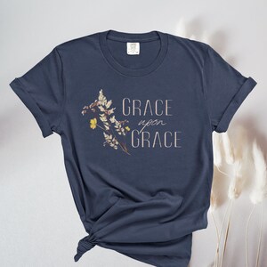 Peut inclure: Un t-shirt bleu marine avec un motif floral et le texte "GRACE upon GRACE" imprim&eacute; sur le devant.