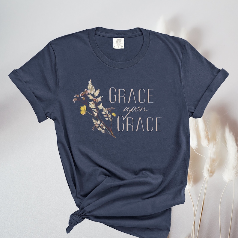 Peut inclure: Un t-shirt bleu marine avec un motif floral et le texte "GRACE upon GRACE" imprim&eacute; sur le devant.