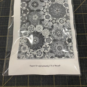 May include: A black and white quilt pattern called "Minuet" by The Darty Kite Pattern Co. The pattern is for a quilt measuring 53 inches by 61 inches. The pattern is for English Paper Piecing or Hand Sewing. The pattern is designed by Leslie Guyton. The image shows a portion of the quilt pattern. The text "Papers for approximately 1/4 of the quilt" is at the bottom of the image.