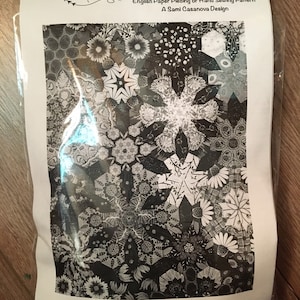 May include: Black and white quilt pattern for Asterisms, a 73x77 inch quilt design by Sami Casanova. The pattern includes a close-up of a section of the quilt with a variety of star-shaped and floral motifs. The text "Papers for approximately 1/4 of the quilt" is at the bottom of the image.