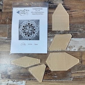 May include: A clear plastic quilting template set with a paper pattern. The paper pattern is in a plastic sleeve and features a black and white floral design. The templates are various geometric shapes, and the text "Compass Garden" is visible.