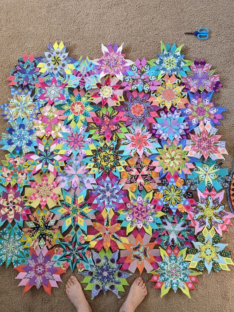 Peut inclure: Une collection de blocs de courtepointe en forme d'&eacute;toile en tissu color&eacute;, dispos&eacute;s en demi-cercle sur un tapis beige. Les blocs de courtepointe sont faits de diff&eacute;rents tissus avec des motifs floraux et g&eacute;om&eacute;triques.